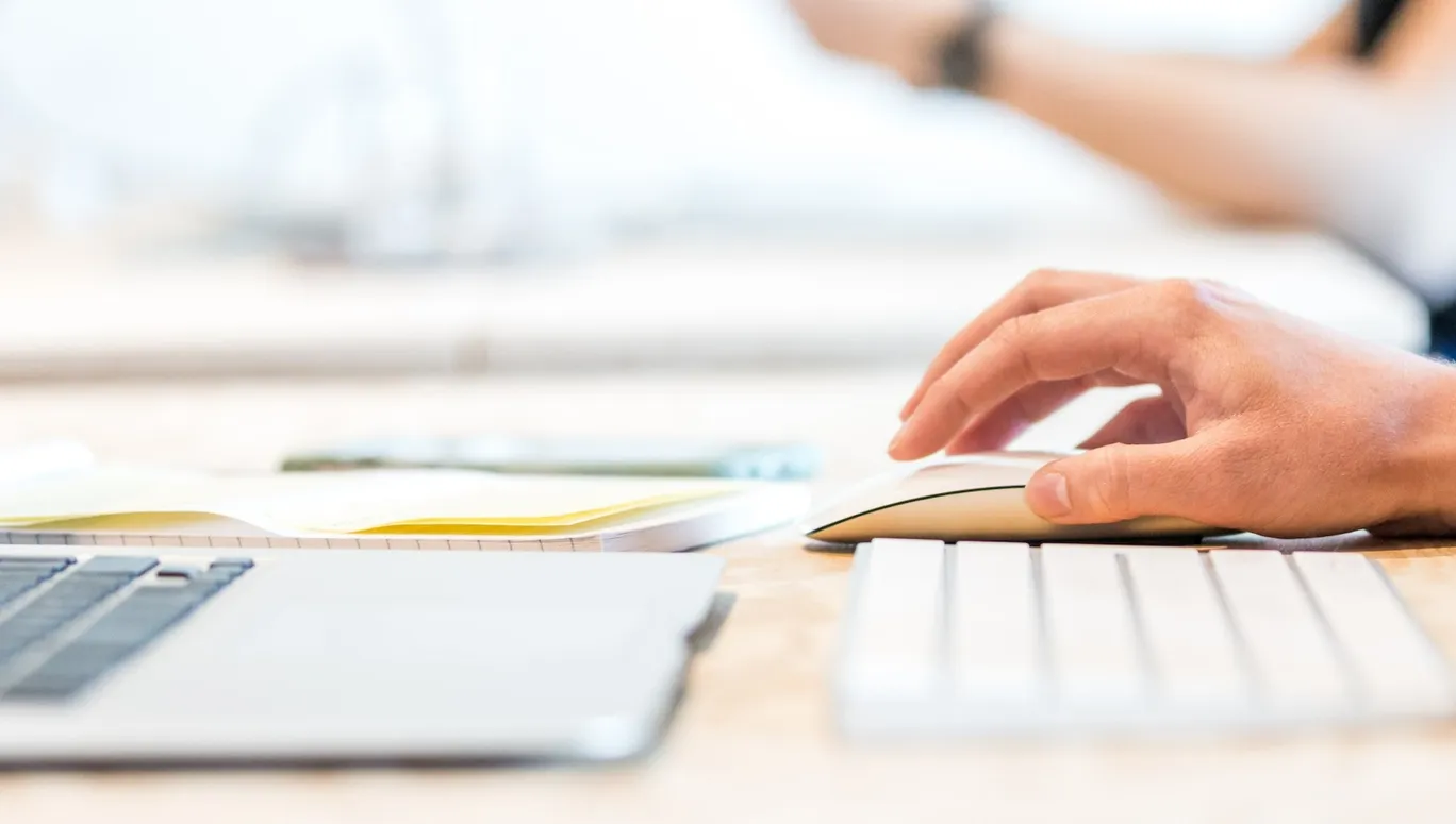 Close up of hand moving mouse next to laptop on desk.