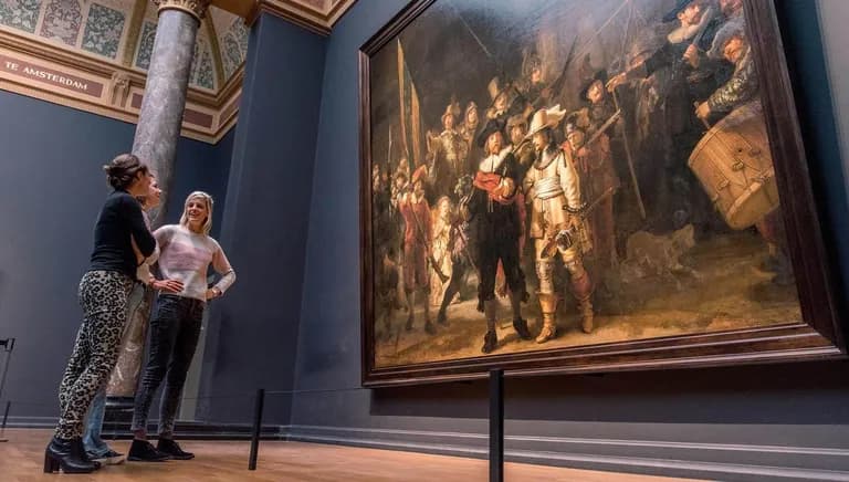 Three women gathered around Rembrandt's Nachtwacht (Nightwatch) painting in the Rijksmuseum.