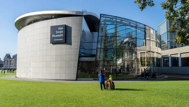 A person with a person in a wheelchair admiring the Van Gogh Museum at a sunny Museumplein.