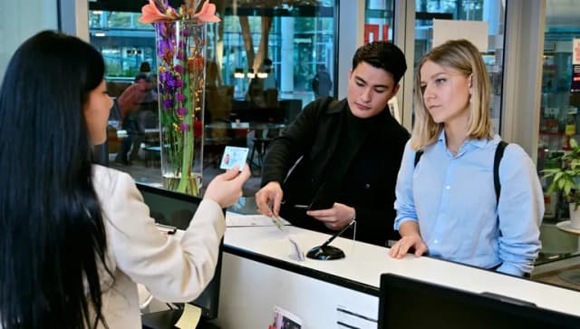 Woman and man at the desk at the INAmsterdam offices. Employee checking id card