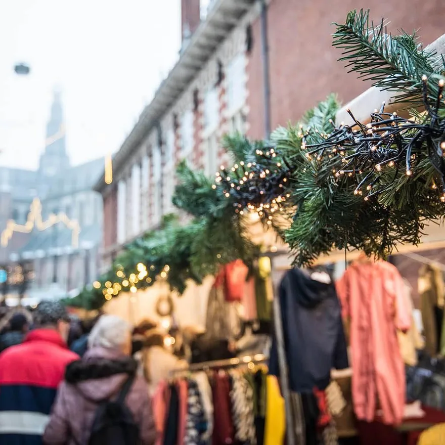 Christmas market in Haarlem. With a close-up of a pine branch covered in Christmas lights with a market and church tower in the background.