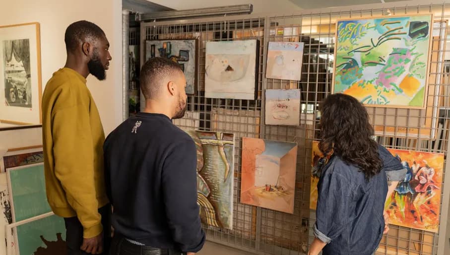 Two men visit the art loan of CBK Zuidoost and are listening to the story of the museum employee.
