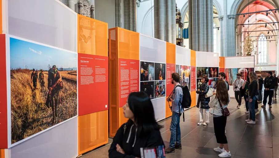 Visitors looking at photos in exhibition at World Press Photo 2023 in De Nieuwe Kerk