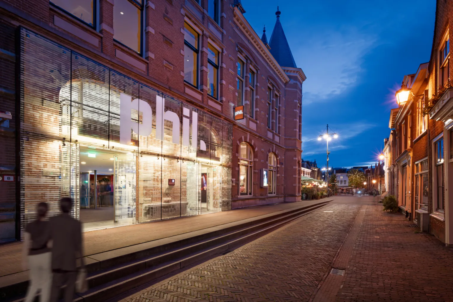 Couple walking past the exterior of PHIL Haarlem concert hall at night