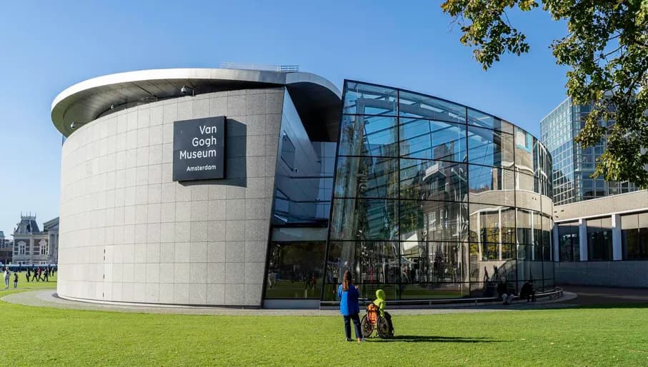 A person with a person in a wheelchair admiring the Van Gogh Museum at a sunny Museumplein.